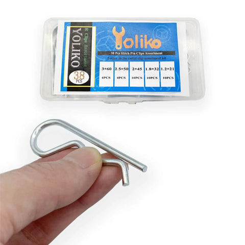 Hand holding component of 38 Piece Hitch Pin Clip Set With Five Sizes For Trailer And Tractor Applications Including Hair Pins R Clips Retaining Pins Spring Clips And Dolly Pin Replacement Kit By Yoliko, product box in background.