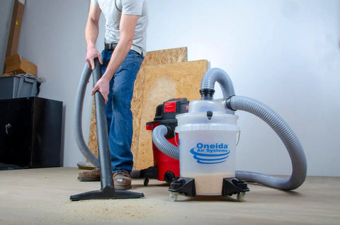 Dust Deputy Low Profile Space Saving Deluxe Lid Dust Separator Kit With Clear Five Gallon Bucket Three Foot Hose Two Point Five Inch Adapter And Mounted Casters For Shop Wet Dry Vacuums in use in a workshop.