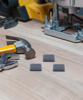 12 Pack PTFE Furniture Sliders for Carpet, Quiet Chair Glides and Table Feet Pads on a wooden surface with tools nearby.