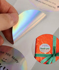 Thank You Stickers For Packaging And Gift Wrapping, shiny label being peeled and applied to a gift box with ribbon