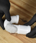 Hands applying Fix It Multi Purpose Epoxy Putty 4 Oz for Quick Leak Sealing on a white pipe joint, beige-gray color visible.