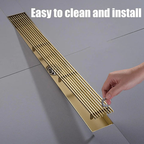 Slick Rectangular Shower Trench Drain With Stainless Steel Grate And Bamboo Hair Strainer shown being installed, features gold finish.