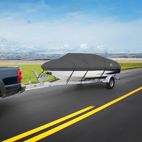 A truck towing a boat with a heavy-duty, black stormpro ski & wakeboard tower cover on a highway, clear sky, and open field backdrop.