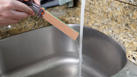 Dia Fold Handy Portable Pocket Diamond Sharpener being rinsed under a kitchen tap, foldable with color-coded sides.