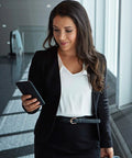 Person in business attire holding a smartphone in a modern office environment, smiling while using technology for communication.