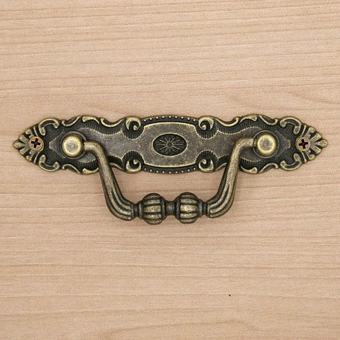 Close-up of a vintage antique brass bail pull on a wooden surface; Six Pack Vintage Antique Brass Bail Pulls For Drawers Cabinets Dressers Cupboards Set Featuring 4.1 Inch Length And 1.5 Inch Height Inter Hole Spacing 3.5 Inches Made From Zinc Alloy With Distressed Finish Retro Rustic Hardware