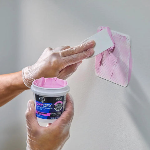 Person applying DryDex Spackling Wall Repair Patch Kit with pink to white dry time indicator on wall, 8 oz container visible