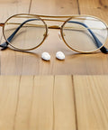 Push In Silicone Nose Pads For Glasses 50 Pack Non Slip Waterdrop Cushions on wooden surface next to stylish eyewear.