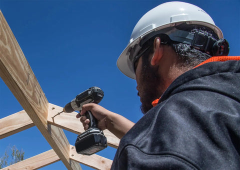 Image of a person using a drill on wood beams, demonstrating Heavy Duty Framing Screws Three Inch Long With Six Lobe Drive And Sharp Sawtooth Tip For Smooth Sailing On Any Wood Project Low Profile Tan Head Bulk Carton Holding One Thousand Top Notch Fasteners.