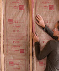 Pro Grade R13 Kraft Fiberglass Roll Insulation Real Deal For 2x4 Walls, woman installing insulation in wall framing.