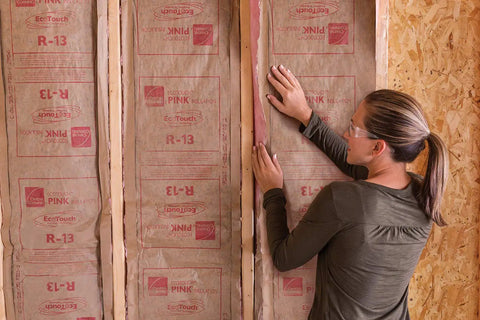 Pro Grade R13 Kraft Fiberglass Roll Insulation Real Deal For 2x4 Walls, woman installing insulation in wall framing.