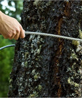 Heavy Duty 8mm Wire Rope Cable For Zip Line And Outdoor DIY Five Sixteenth Inch Stainless Steel Cable With Seven Thousand Lbs Breaking Strength Rust Resistant 304 Stainless Steel For Backyard Adventures And Industrial Grade Projects being held taut against a tree trunk in a forest setting.