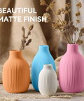 Four vases with a matte finish in orange, blue, white, and pink, displayed with dried flowers on a neutral background.