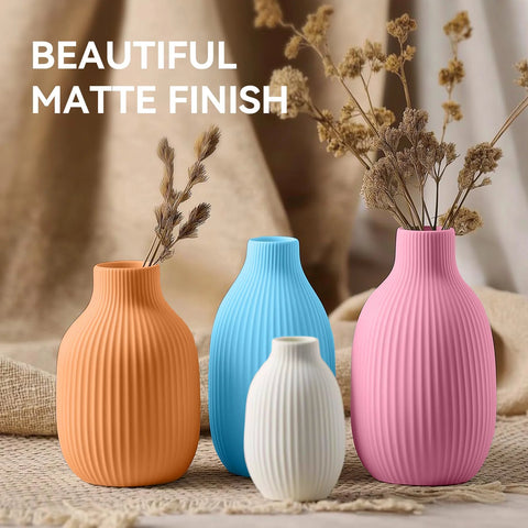 Four vases with a matte finish in orange, blue, white, and pink, displayed with dried flowers on a neutral background.