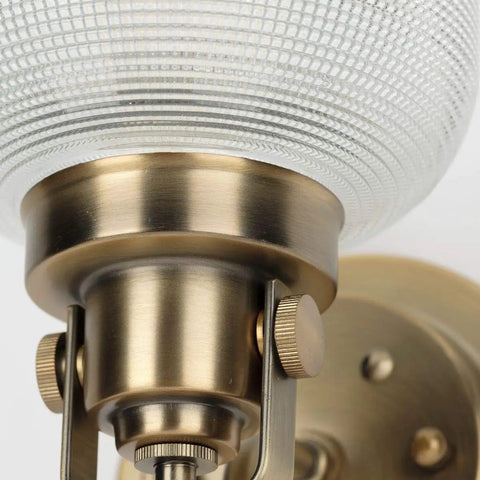 Close-up of Archie Collection Clear Double Prismatic Glass Coastal Bath Vanity Light Fixture in Vintage Brass Finish