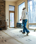 Worker using X Board Paint and Remodel Surface Protector Heavy Duty Breathable Floor Shield 35 Inch by 100 Feet Roll during renovation.