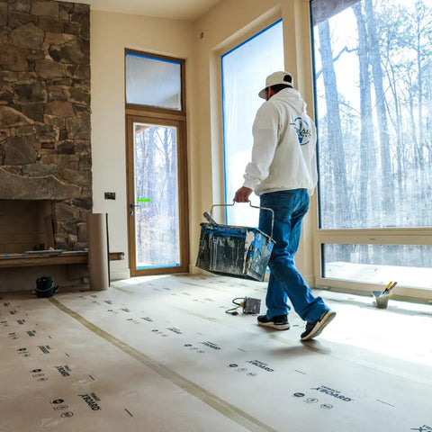 Worker using X Board Paint and Remodel Surface Protector Heavy Duty Breathable Floor Shield 35 Inch by 100 Feet Roll during renovation.