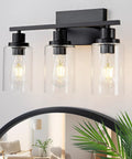Top Shelf Matte Black Three Light Bathroom Vanity Fixtures With Clear Glass Shades, modern farmhouse design, mounted above mirror.