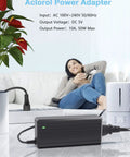 Beefy 5V 10A 50W LED Power Supply Adapter with 5.5x2.1mm plug and safety protections on table, woman relaxing in background.
