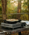 Butane Camp Stove With Flat Top Griddle Included Portable Piezo Ignition Diecast Aluminum Nonstick Coating Tent Camping Stove For Outdoor Cooking And Kitchen Powerful Burners For Grilling Boiling on a table with pancakes.