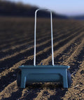Walk Behind Seed Spreader 12 Liter Hand Push Garden Seeder Broadcast and Drop Spreader on plowed field background