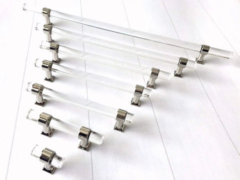 Assorted sizes of sleek Lucite acrylic cabinet pulls in clear chrome finish displayed on a surface, polished silver handles.