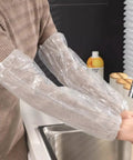 Person wearing Disposable Arm Sleeve Covers 200 Pack Clear Plastic Sleeves For Painting, Repairs, Cleaning, And Tattooing.