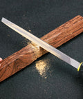 Mini 140mm metal rasp file with yellow-black handle used to shave wood on a dark work surface