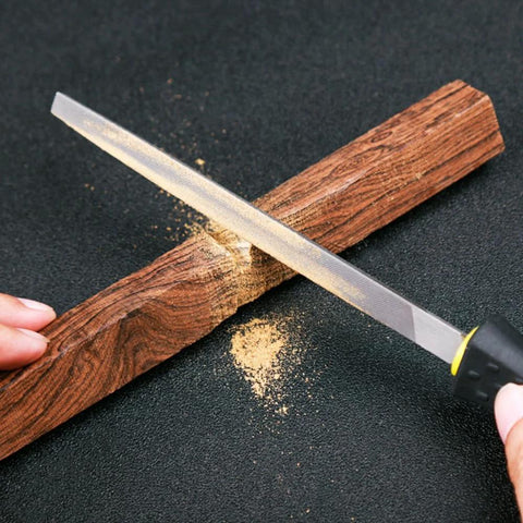 Mini 140mm metal rasp file with yellow-black handle used to shave wood on a dark work surface