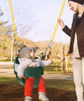 Kid Friendly Toddler Swing Seat With Coated Chains And Heavy Duty High Back Bucket For Outdoor Backyard Play Includes Tree Straps And Hooks For Swing Sets, child seated in green swing with yellow chains, woman assisting.