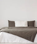 Modern bedroom with grey and white bedding, wooden side table, white lamp, and minimal decor in a cozy setting.