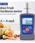 Digital Fruit Hardness Tester Handheld Sclerometer Penetrometer with clear display on a kitchen counter beside fresh fruits.