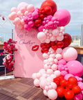 Balloon arch made of 66 Piece 12 Inch Hot Pink And Red Balloons Set With White And Gold Confetti for party decor on a rooftop.