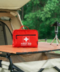 Rhino Rescue 240-Piece All-Purpose First Aid Kit, red, on camping table beside lantern.