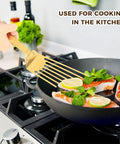 Snailhouse Slotted Spatula, gold stainless steel high-heat fish turner, angled in skillet.