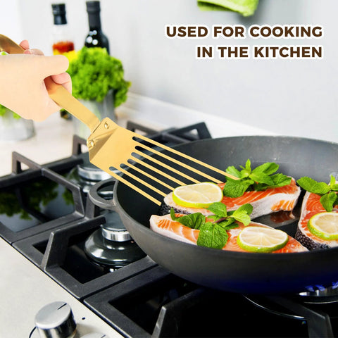 Snailhouse Slotted Spatula, gold stainless steel high-heat fish turner, angled in skillet.
