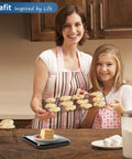 Mother and daughter with cookies, next to 22 Pound Digital Kitchen Scale With 0.1 Ounce And 1 Gram Precision For Cooking And Baking, pro grade.