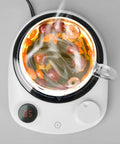 This Solid Electric Mug Warmer Boasts Four Heat Presets To Keep Your Daily Brew Piping Hot All Day Long Featuring Smart Auto Shut Off Protection And Fast Heating With A Sleek White Top For Desk Setup. Glass mug with steaming tea on electric warmer.