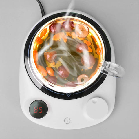This Solid Electric Mug Warmer Boasts Four Heat Presets To Keep Your Daily Brew Piping Hot All Day Long Featuring Smart Auto Shut Off Protection And Fast Heating With A Sleek White Top For Desk Setup. Glass mug with steaming tea on electric warmer.