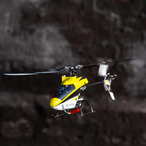 120S2 RC Helicopter BNF With SAFE Technology hovering in air, showcasing carbon fiber airframe and durable polymers against dark background