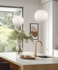 Ceres 14-Inch Mid Century Modern Globe Pendant Light With Frosted Glass Orb Warm Brass Finish in stylish kitchen setting.
