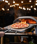 16-inch metal pizza peel with long handle transferring a pepperoni pizza to an outdoor Ooni pizza oven