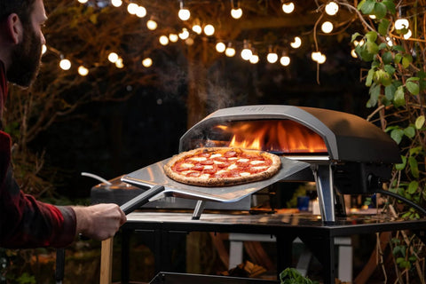 16-inch metal pizza peel with long handle transferring a pepperoni pizza to an outdoor Ooni pizza oven