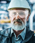 Man wearing Six Pair Set Top Shelf protective Safety Glasses With smart Vitilated Wraparound Frames, hard hat, serious expression.