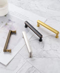 Various metal cabinet handles, including 3 Inch Brushed Gold Cabinet Handles Set, 10 Pack Gold Cabinet Pulls for Cabinets Dresser Cupboard Kitchen Bedroom and Bathroom, Solid Metal Hardware With Smooth Rounded Edges P35 Style Easy Mount, displayed on marble surface.
