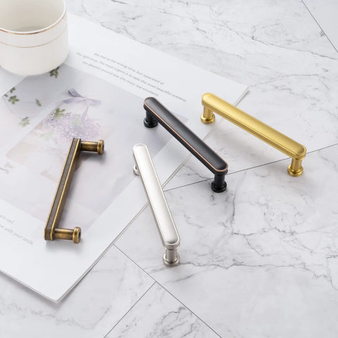 Various metal cabinet handles, including 3 Inch Brushed Gold Cabinet Handles Set, 10 Pack Gold Cabinet Pulls for Cabinets Dresser Cupboard Kitchen Bedroom and Bathroom, Solid Metal Hardware With Smooth Rounded Edges P35 Style Easy Mount, displayed on marble surface.