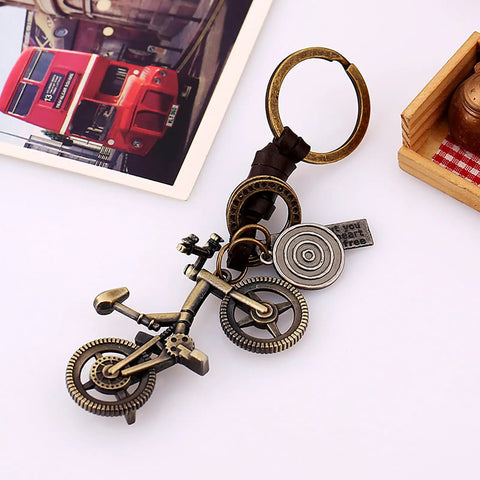 Vintage Leather And Bronze Bicycle Keychain With Metal Wheel And Handlebars Pendant on white surface with a photo in the background