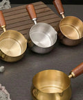 Gold and silver stainless steel espresso measuring cups with wooden handles and V spouts for brewing, 6 oz, 180 ml.