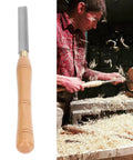 Chisel turning tool with wooden handle and rectangular steel blade for wood lathe turning; wood shavings around.