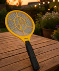 Powerful Handheld Bug Zapper for Home and Outdoors on wooden table, 3-layer grid, yellow plastic, battery-powered, outdoor evening setting